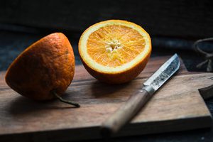 Eine zweigeteilte Orange mit Messer auf einem Brett.